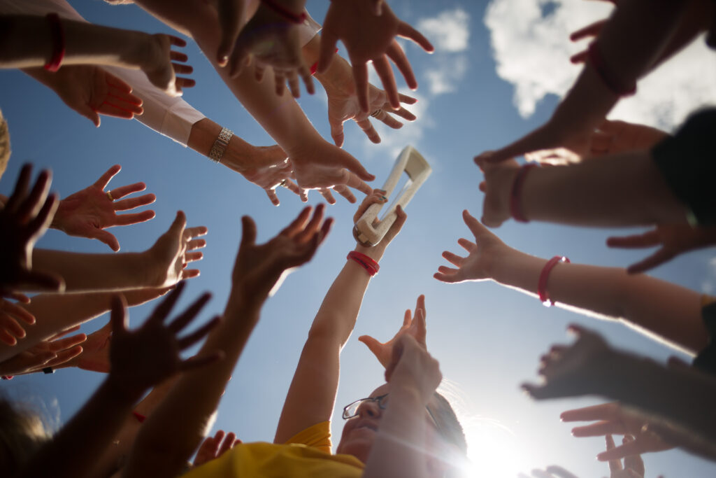 Many hands reaching for an object above.