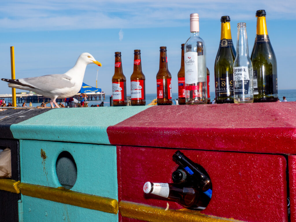 Empty beer and wine bottles stacked for recycling on Brighton beach.