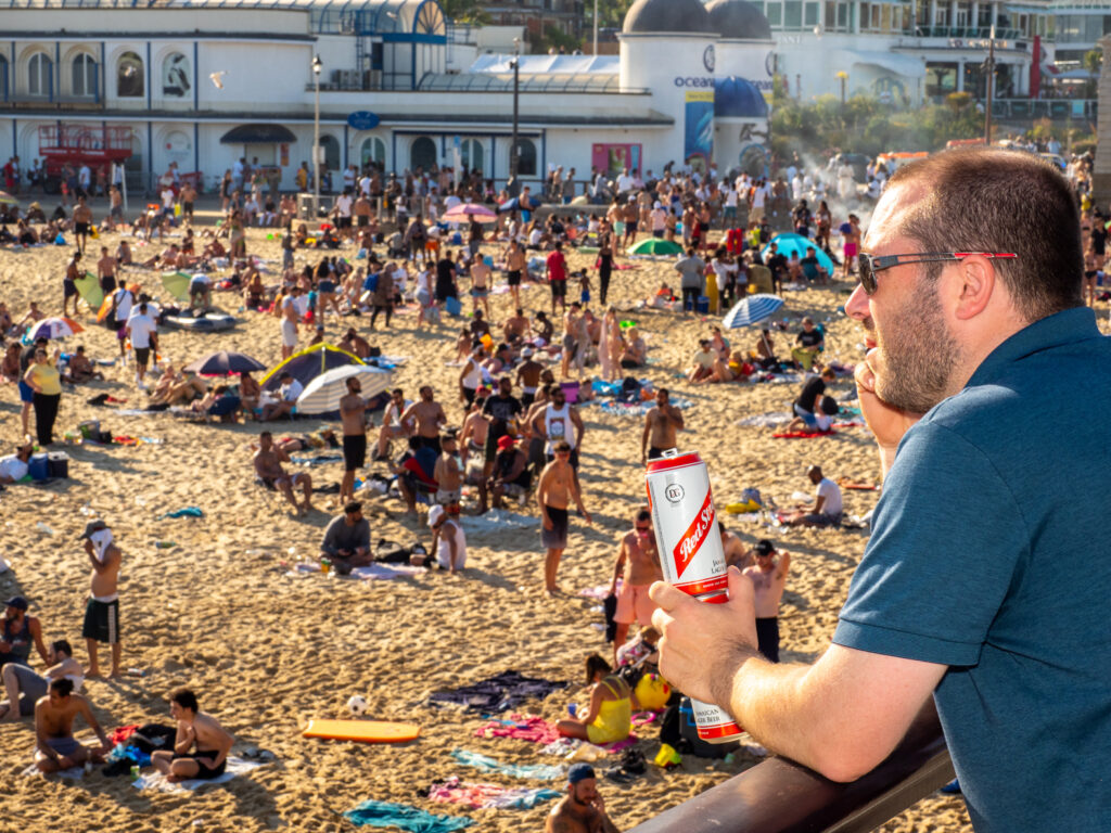 Man with cans of Re Stripe beer on crowded UK beach