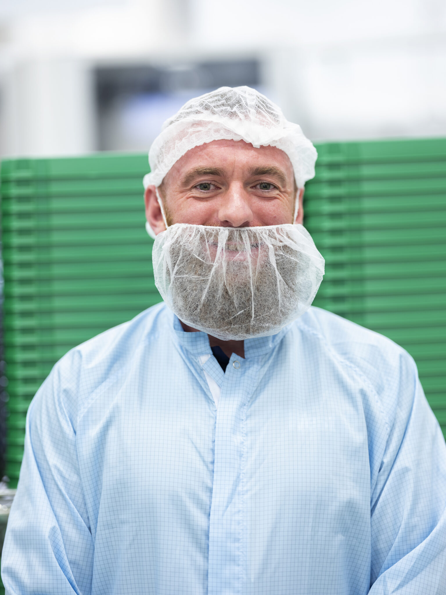 A Happy male employee working at a pharmaceutical factory and looking at the camera smiling wearing protective clothing, hair and beard coverings. multi-location global brand visual library.