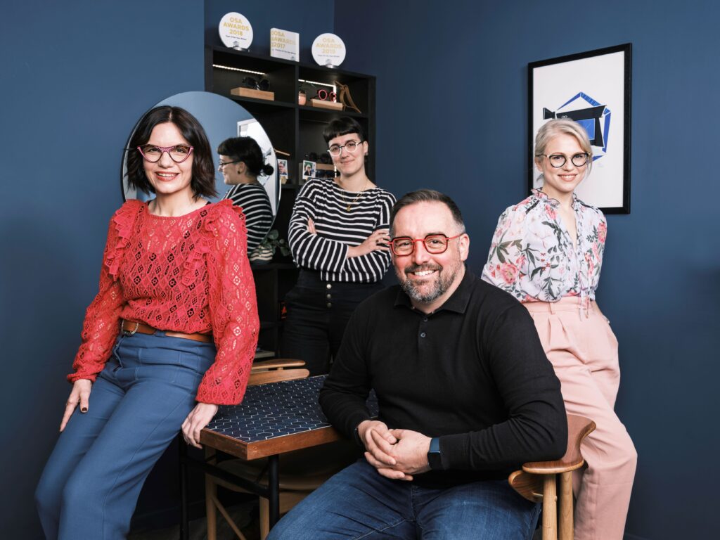 Happy team of opticians smiling at the optometry office while looking at the camera