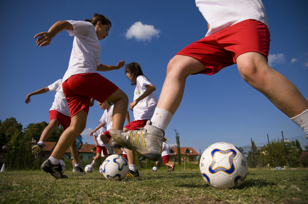 Girls in early and mid teens exercising on sports field, improving footwork and dribbling skills.