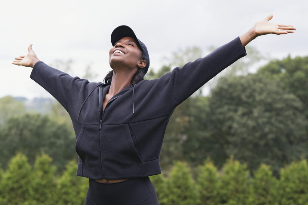 Black woman, freedom and wellness in nature with fitness, health and meditation by outdoor. Woman exercise and open arms in gym clothing and happy with peace by cloudy sky