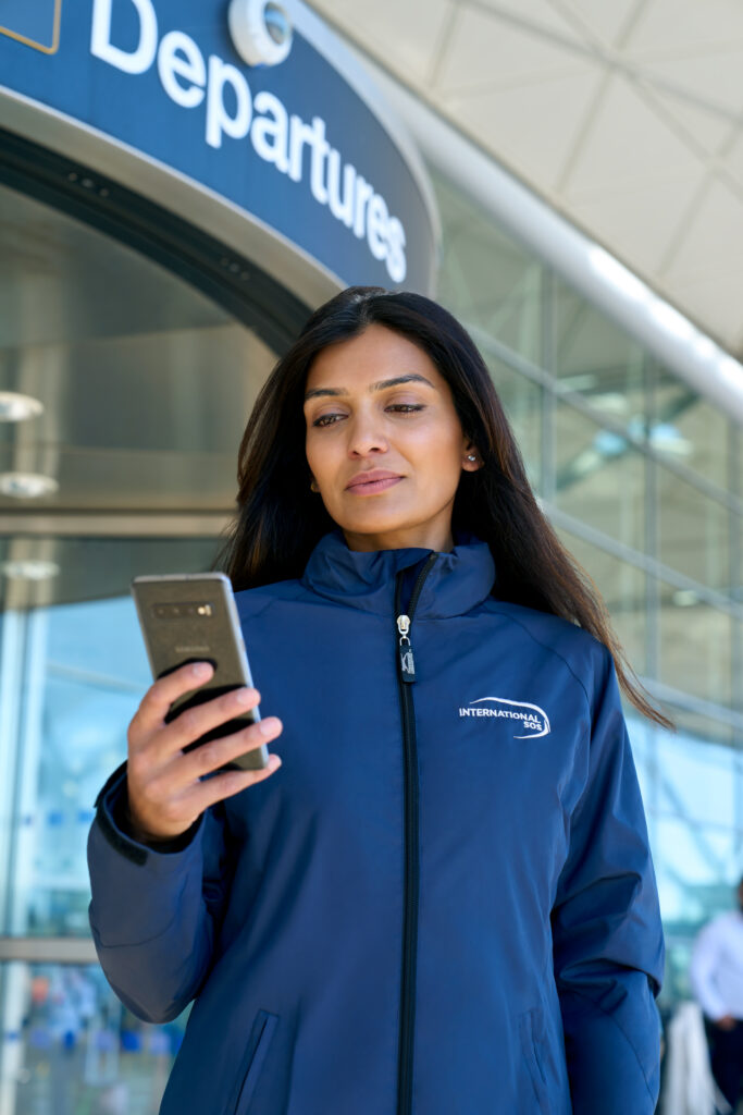 Woman with long dark hair outside airport looking at mobile phone.