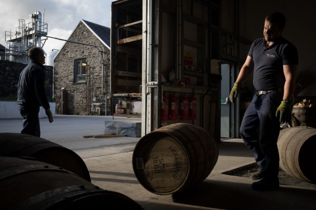 A Caucasian man standing near barrels in a whisky distillery