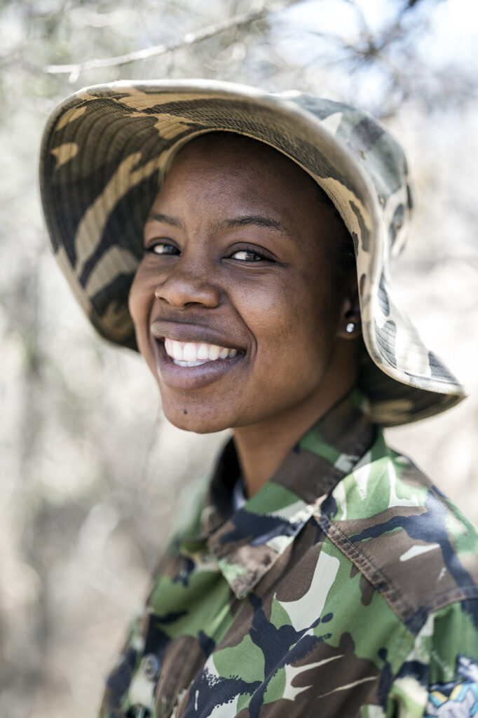 Female warden anti-poaching police female smiles into camera wearing camouflage hat and shirt. 