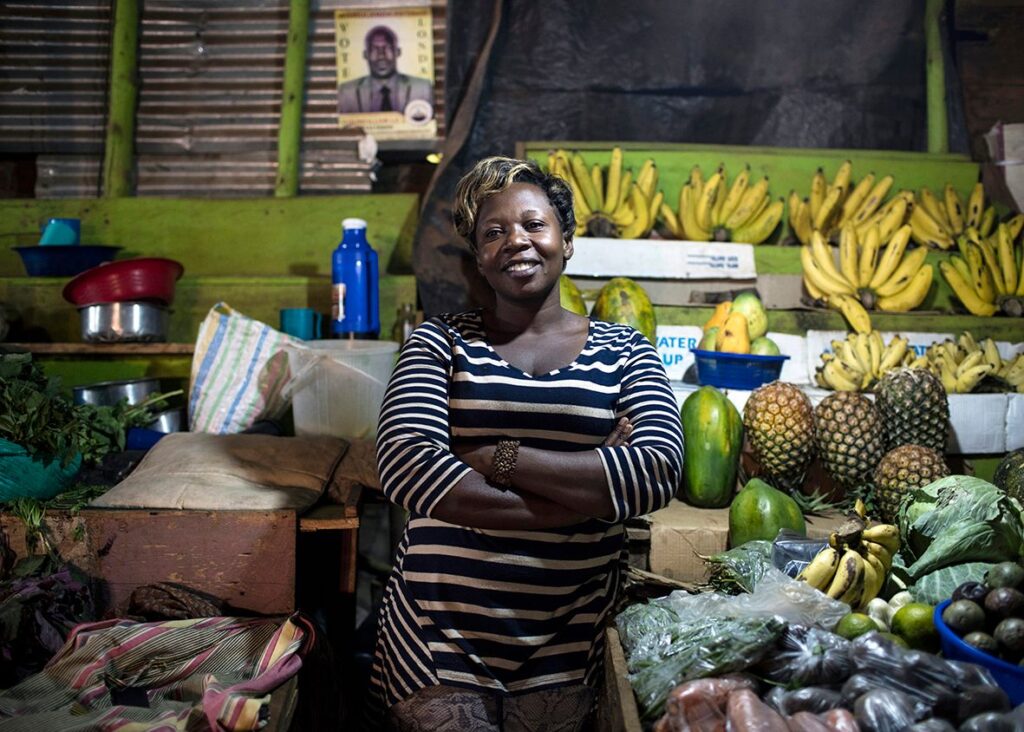 A proud African woman stands in front of her stall of plantain tropical fruit