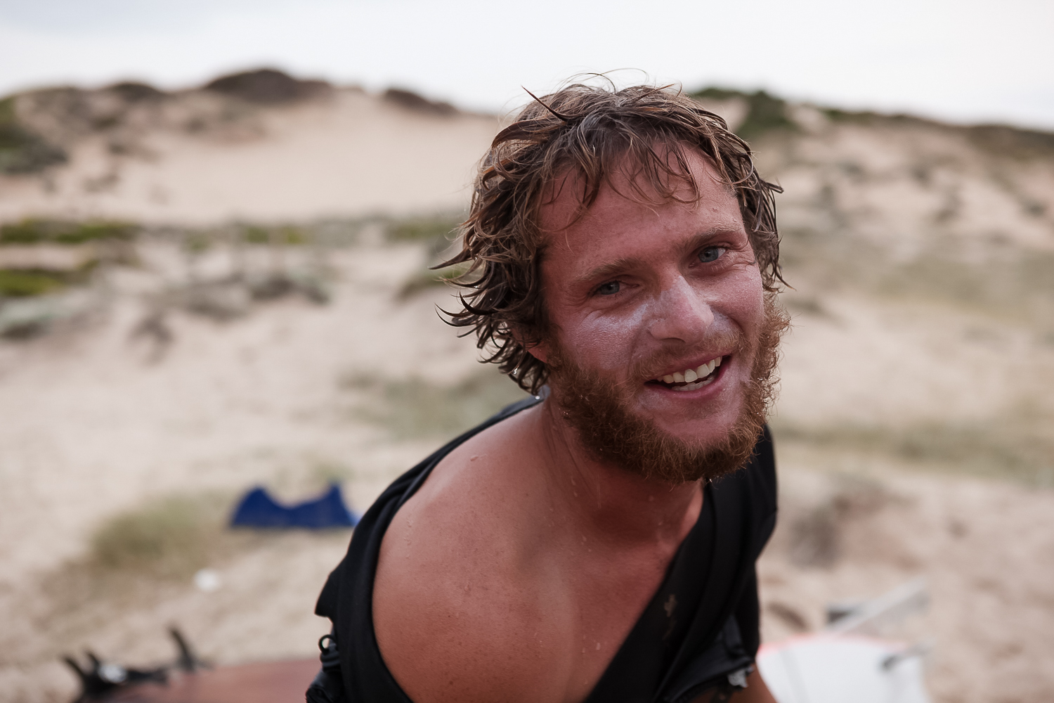 A man with wet hair and beard on the beach.