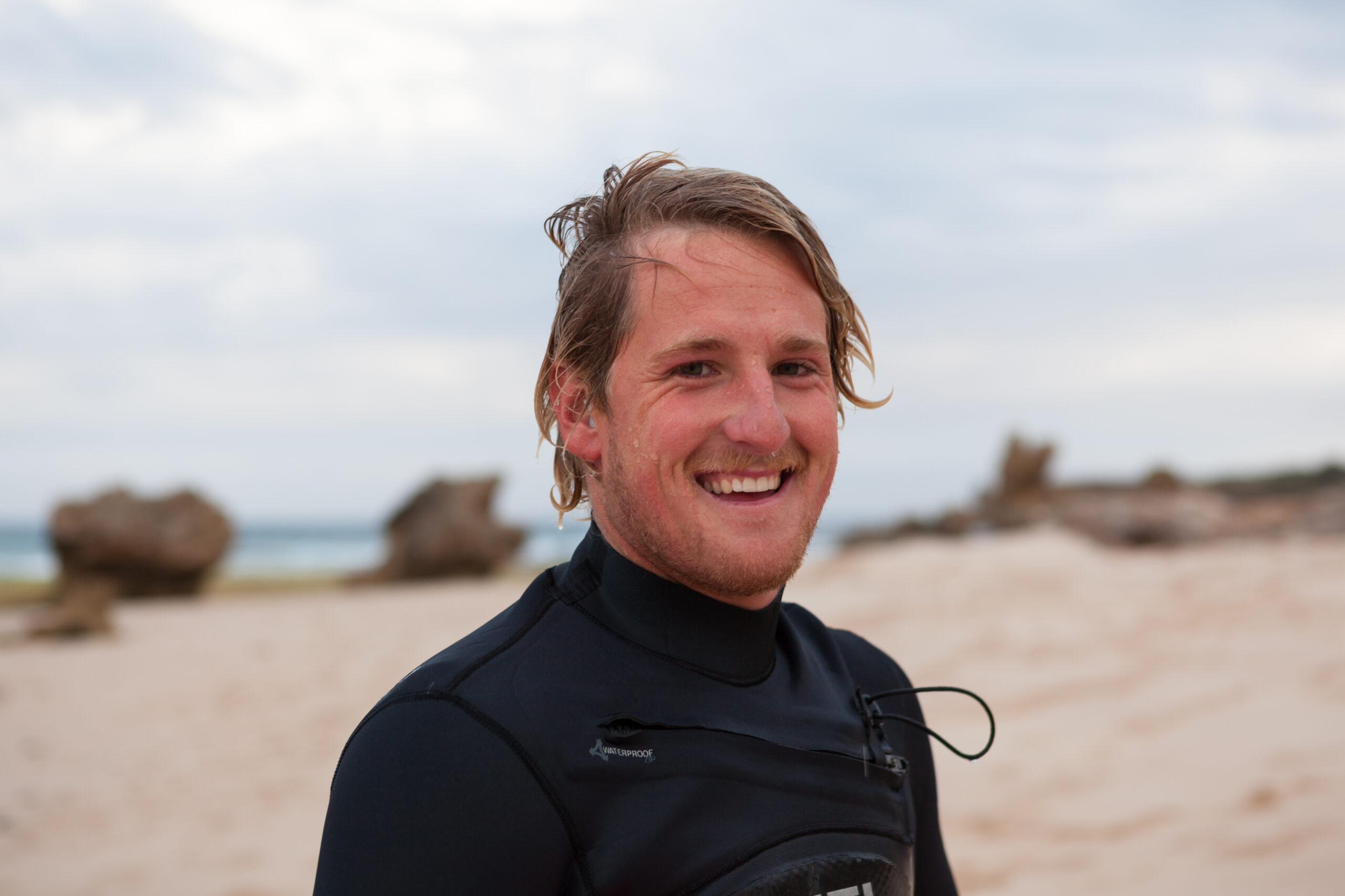 A man in a black wetsuit standing on the beach.