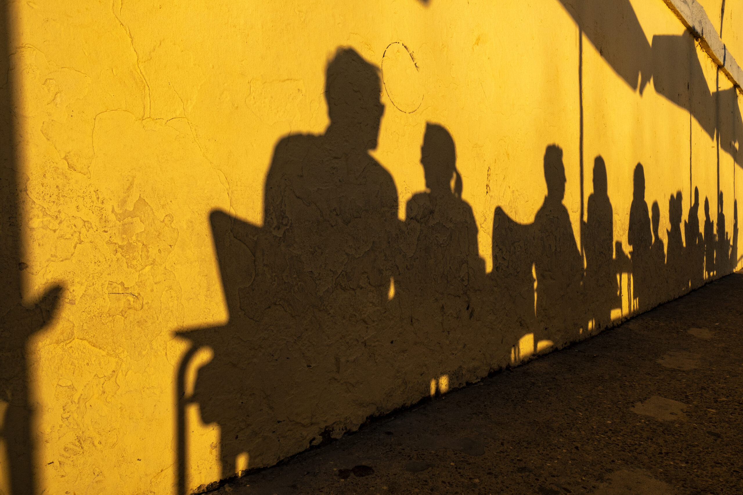 Shadows of people sitting outside at a coffee shop reflecting against a yellow wall. Multi-Location Photography