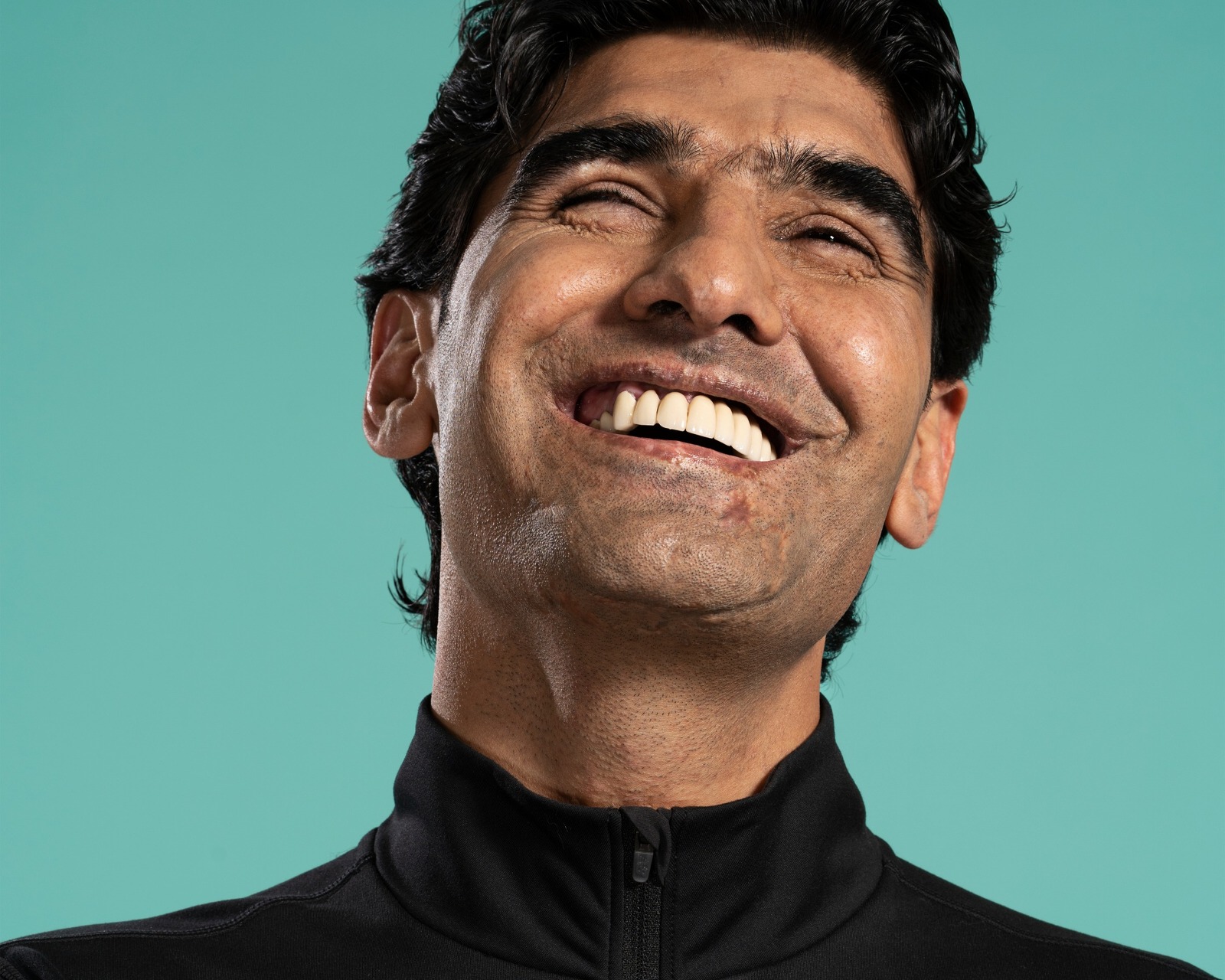 Inclusive photography highlighting diversity and disability in visual culture. Portrait of Wali Noori blinded by a Taliban ambush. wearing a black poloneck jumper, photographed in a studio against green backdrop. sustainable campaign photography
