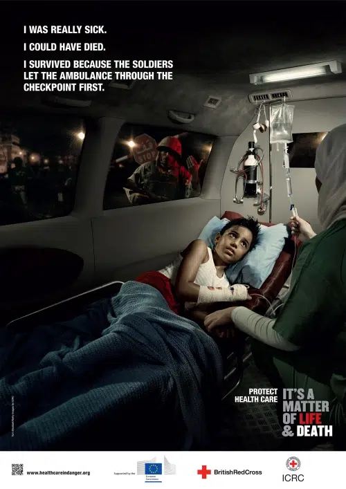 Paramedics treating an injured patient inside an ambulance at a checkpoint, staged for ICRC Health Care in Danger campaign